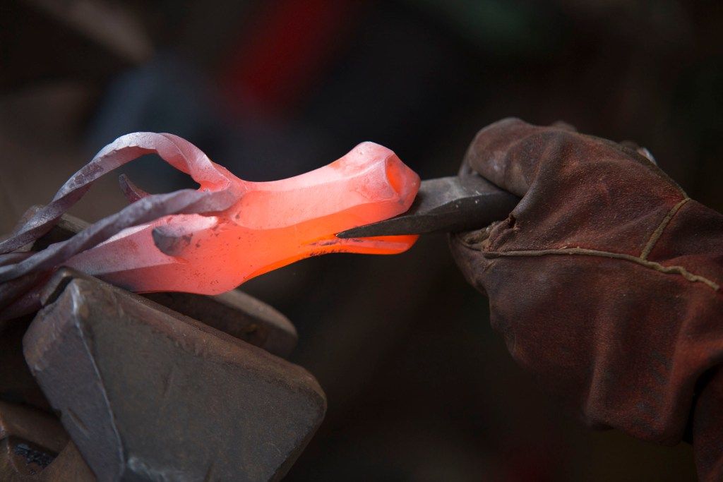 Glowing hot iron being shaped with tongs at the forge